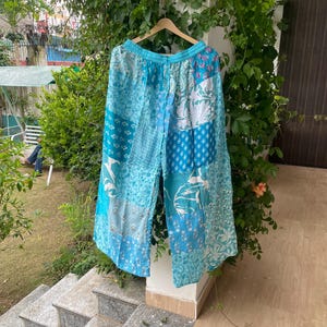Könnte beinhalten: Weit geschnittene Hose mit einem Patchwork-Design in verschiedenen Blau- und Weißtönen. Das Kleidungsstück verfügt über einen elastischen Bund und besteht aus mehreren Stoffbahnen, die jeweils unterschiedliche florale und geometrische Muster zeigen.