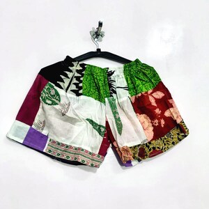 Pode incluir: Calções com um design de patchwork feito de vários retalhos de tecido. A peça apresenta uma mistura de cores incluindo verde, branco, preto, roxo e vermelho escuro, com padrões como motivos florais, bordas geométricas e ilustrações de árvores.