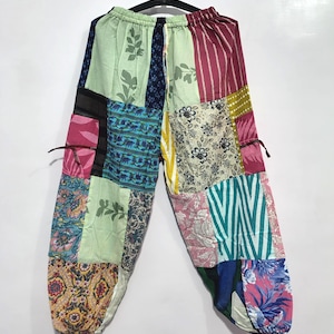 May include: Patchwork trousers featuring an elastic waistband and a variety of colorful fabric panels. The design includes diverse patterns such as floral, striped, and botanical prints in shades of pink, blue, green, yellow, and white.