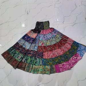 May include: A floor-length skirt featuring a tiered, patchwork design with a smocked elastic waistband. The garment is composed of various fabric panels in diverse colors including pink, blue, green, and dark tones, all displaying intricate paisley and floral patterns throughout the entire piece.