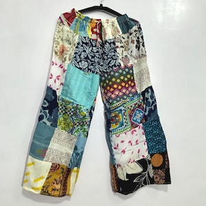 Può includere: Pantaloni a gamba larga con un design patchwork composto da vari quadrati di tessuto in molteplici colori, tra cui blu, giallo, bianco e nero. Il capo presenta una vita elasticizzata con coulisse e mostra diversi motivi floreali, geometrici e astratti su tutta la superficie.
