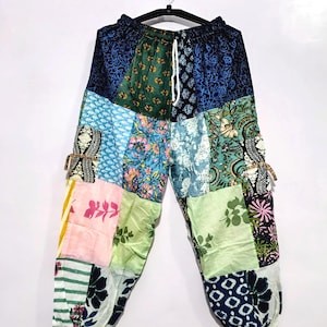May include: Patchwork trousers featuring a variety of floral and geometric patterns in shades of blue, green, pink, and white. The trousers have an elastic waistband with a white drawstring and elasticated cuffs at the ankles, constructed from multiple fabric panels.