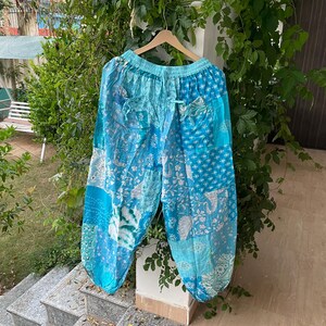 May include: Loose-fitting pants featuring a patchwork design in various shades of blue and white. The garment has an elastic waistband with a drawstring, a relaxed silhouette, and gathered cuffs at the ankles, showcasing a mix of floral and paisley patterns.