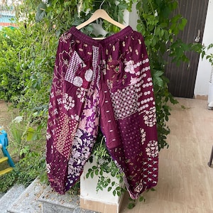Könnte beinhalten: Weit geschnittene Hose in tiefen Violett- und Kastanientönen mit einem Patchwork-Design aus verschiedenen Blumen- und geometrischen Mustern. Das Kleidungsstück hat einen elastischen Bund mit Kordelzug und geraffte Beinabschlüsse.