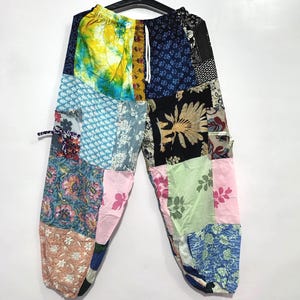 May include: Patchwork pants featuring a variety of colorful fabric squares with floral, botanical, and abstract patterns. The garment includes an elastic waistband with a white drawstring, side pockets, and a loose, relaxed fit throughout the legs.