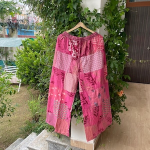 May include: Wide-leg pants featuring a patchwork design in various shades of pink. The garment is constructed from multiple fabric panels with diverse patterns, including floral, leaf, and geometric prints, and includes an elasticized waistband.
