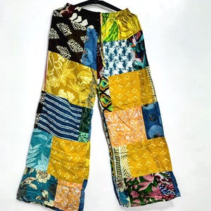Pode incluir: Calças de perna larga com um design de patchwork composto por vários quadrados de tecido em tons de amarelo, azul, verde e castanho. A peça apresenta uma mistura de padrões florais, geométricos e às riscas, com uma cintura elástica.