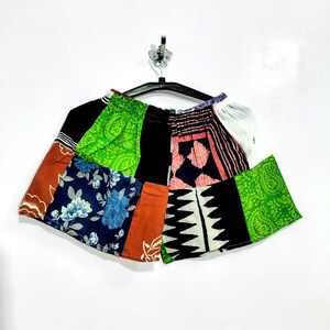 May include: A pair of shorts constructed from various fabric patches featuring diverse patterns including green paisley, blue floral prints, black and white geometric shapes, and solid orange and black panels with an elasticized waistband.