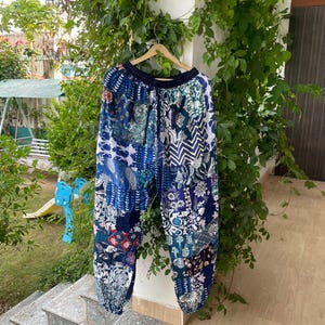 May include: Loose-fitting trousers featuring a patchwork design in various shades of blue and white. The pants have an elasticized waistband with a drawstring, a relaxed silhouette, and a mix of floral, geometric, and abstract patterns throughout.
