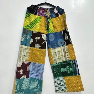 Könnte beinhalten: Weite Hose mit einem Patchwork-Design aus verschiedenen Stoffquadraten in Senfgelb, Petrol, Dunkelblau, Braun und Grün. Das Kleidungsstück verfügt über einen elastischen Bund mit Kordelzug und zeigt verschiedene florale und geometrische Muster.