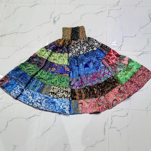 Puede incluir: Una falda larga de niveles con cintura elástica fruncida y un diseño de patchwork vibrante. La falda está compuesta por múltiples paneles horizontales que muestran varios patrones coloridos de cachemira, florales y geométricos en tonos azul, verde, rosa y negro.