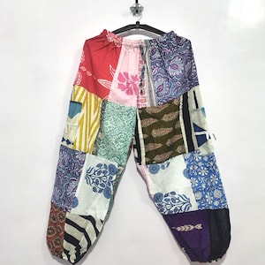 May include: Loose-fitting trousers featuring a patchwork design composed of various fabric panels in red, pink, green, blue, white, and purple. The pants include an elasticized waistband and gathered cuffs at the ankles, showcasing diverse floral and geometric patterns.
