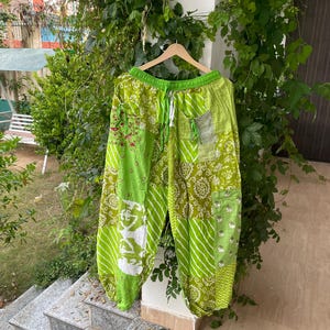 May include: A pair of lime green patchwork pants featuring a variety of printed patterns including stripes, floral motifs, and geometric shapes. The pants have an elastic waistband with a drawstring, side pockets, and elasticized cuffs at the ankles.