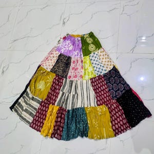 Puede incluir: Una falda larga de paneles con un diseño de patchwork que incluye diversas telas en colores verde oliva, amarillo mostaza, rojo oscuro, negro, blanco y morado, con variados estampados florales, geométricos y abstractos.