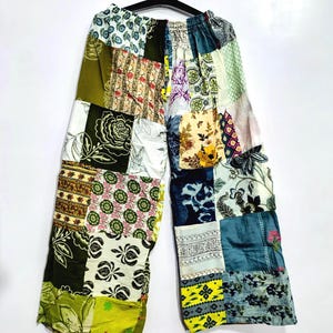 May include: Wide-leg trousers featuring a patchwork design composed of various fabric squares in shades of olive green, yellow, blue, white, and black. The garment includes an elasticized waistband and displays diverse floral, geometric, and abstract patterns.