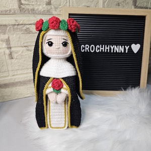 Puede incluir: Muñeca de ganchillo hecha a mano de una monja, vestida con un hábito negro con ribetes dorados y una toca blanca. La muñeca tiene una corona de rosas rojas y sostiene una rosa roja. El texto "CROCHHYNNY" es visible.