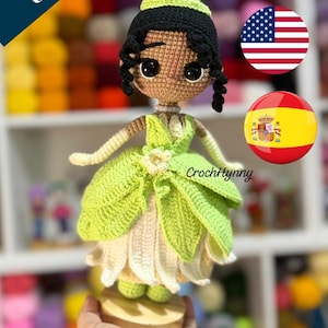 May include: A crochet amigurumi doll of Tiana with black hair, a yellow crown, and a green and white leaf-patterned dress. The text 'Patrón amigurumi Crochet Pattern' and 'TIANA' are visible. The doll features large dark eyes and a pearl necklace.