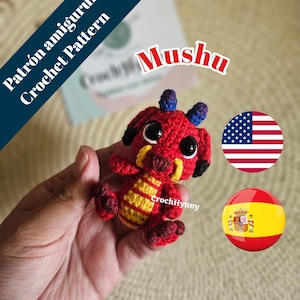 May include: A red and yellow crocheted dragon toy with large black eyes and blue horns. The dragon is labeled "Mushu" and is a handmade amigurumi. The image also includes a US flag and a Spanish flag.