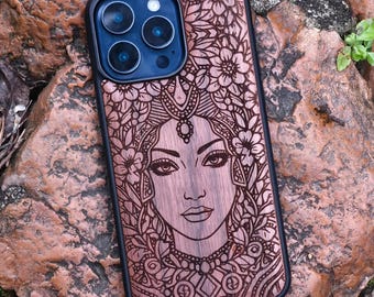May include: A wooden phone case with a detailed engraved design of a woman's face surrounded by flowers. The case has a black border and a blue camera lens area. The wood has a reddish-brown hue.