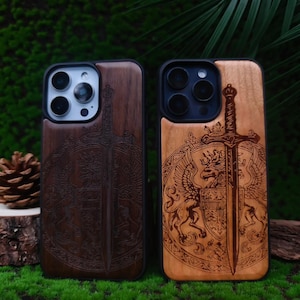May include: Two wooden phone cases with intricate sword and shield designs. One case is dark brown, the other is light brown. Both cases have a black border and are set against a green, natural background.