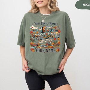 May include: A moss green short-sleeve t-shirt featuring a graphic print with the text "YOUR FAMILY NAME NEW ENGLAND FAMILY AUTUMN ADVENTURE YOUR NAME". The design includes illustrations of a lighthouse, autumn foliage, houses, and a pumpkin.
