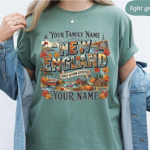 May include: A light green t-shirt featuring a graphic print with the text Your Family Name, New England, Family Autumn Adventure, and Your Name. The design includes a lighthouse, a ship, a covered bridge, houses, pumpkins, and autumn leaves.