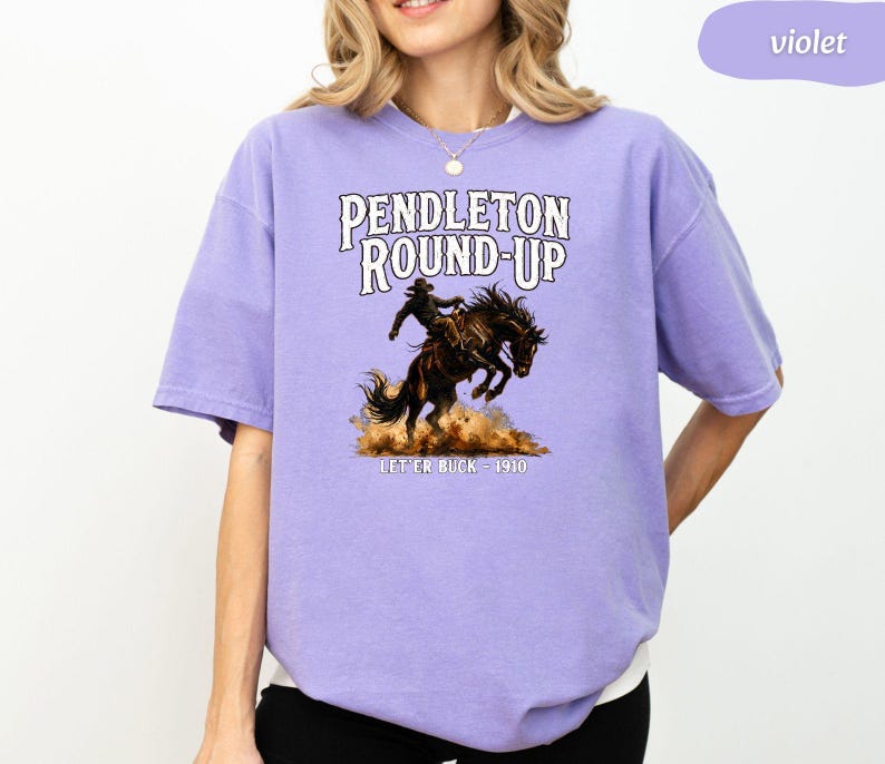 May include: A lilac-coloured t-shirt with the text "PENDLETON ROUND-UP" above a rodeo illustration of a cowboy on a bucking bronco. The text "LET ER BUCK - 1910" is below the illustration.