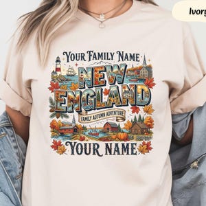 May include: An ivory t-shirt featuring a colourful graphic print with the text "YOUR FAMILY NAME", "NEW ENGLAND", "FAMILY AUTUMN ADVENTURE", and "YOUR NAME". The design includes illustrations of a lighthouse, a ship, autumn leaves, and cabins.