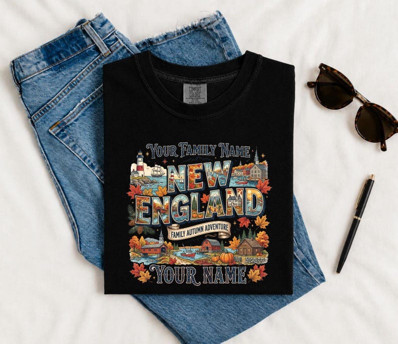 May include: A black t-shirt featuring a graphic with the text "YOUR FAMILY NAME", "NEW ENGLAND", "FAMILY AUTUMN ADVENTURE", and "YOUR NAME". The design includes illustrations of a lighthouse, a ship, autumn leaves, a pumpkin, and buildings.