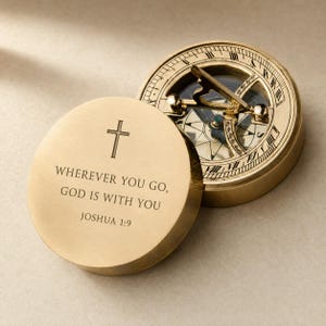 Può includere: Una bussola rotonda in ottone con coperchio rimovibile. Il coperchio presenta una croce incisa e il testo: WHEREVER YOU GO, GOD IS WITH YOU JOSHUA 1:9. L'interno della bussola mostra un quadrante circolare con numeri romani e un ago.
