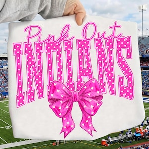 Könnte beinhalten: Ein weißes T-Shirt mit dem Text Pink Out INDIANS in großen, pinkfarbenen Blockbuchstaben mit Punkten. Unter dem Text befindet sich eine große, leuchtend pinke Schleifengrafik mit einem Muster aus kleinen weißen Herzen auf der Vorderseite.