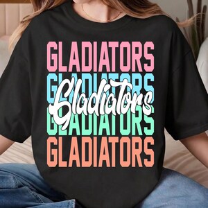 May include: Black t-shirt with the word "GLADIATORS" in a stacked design. The word is in a mix of colors: pink, light blue, white, teal, and orange. The shirt has short sleeves and a crew neck.