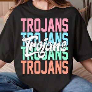 May include: Black t-shirt with the word "Trojans" in pink, light blue, white, light green, and orange block letters. The word "Trojans" is repeated multiple times in a stacked design.