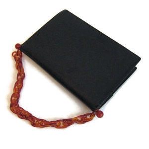 May include: A black leather clutch purse with a brown plastic chain strap.