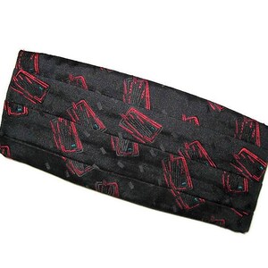 May include: Black cummerbund featuring a repeating design of red and teal rectangles. The pleated cummerbund has a subtle dotted texture. This formal accessory adds a splash of colour to any outfit.