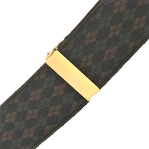 May include: A close-up of a black and brown argyle patterned suspender with a gold-coloured metal clasp. The suspender is angled across a white background.
