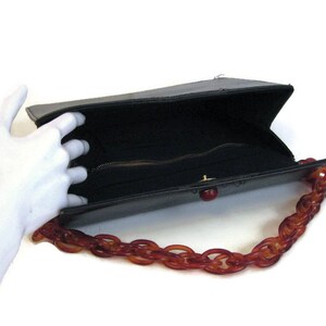 May include: A black leather handbag with a brown plastic chain strap. The bag is open and the inside is lined with black fabric. The bag has a zipper closure.