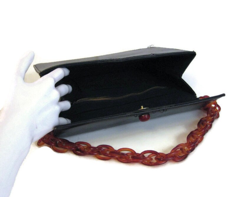 May include: A black leather handbag with a brown plastic chain strap. The bag is open and the inside is lined with black fabric. The bag has a zipper closure.