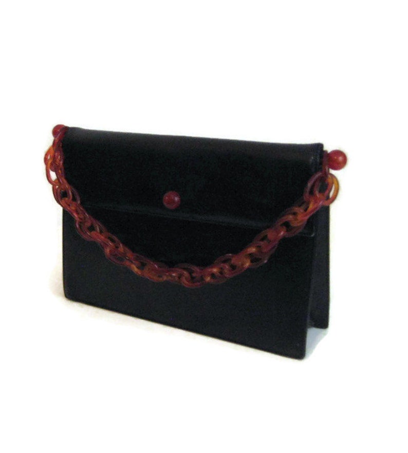 May include: A black leather clutch purse with a red and orange plastic chain strap.