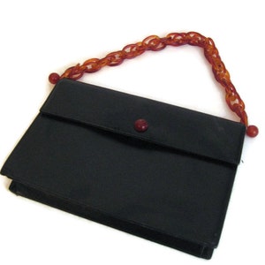 May include: A black leather clutch purse with a red button closure and a brown plastic chain strap.