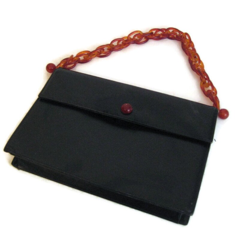 May include: A black leather clutch purse with a red button closure and a brown plastic chain strap.