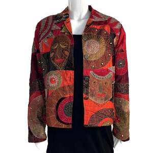 May include: A red, black and gold quilted jacket with a unique design featuring embroidered circles and stylised faces. The jacket has a button closure and long sleeves.