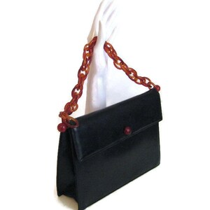 May include: A black leather handbag with a flap closure and a long, brown plastic chain strap. The strap has red plastic beads at the ends.