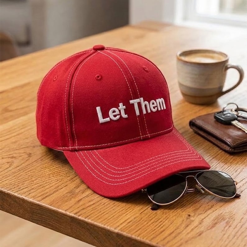Puede incluir: Una gorra de b&eacute;isbol de color rojo brillante con costuras blancas en contraste y el texto Let Them bordado en blanco en el panel frontal. La gorra cuenta con una corona estructurada, una visera curva y ojales para la ventilaci&oacute;n.