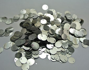 May include: A pile of silver round sequins with a small hole in the center of each sequin.
