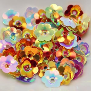 May include: A pile of iridescent flower-shaped sequins in various colors, including pink, orange, yellow, and green.