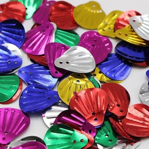 May include: A collection of colorful, metallic seashell-shaped sequins in various colors, including red, green, blue, pink, silver, and gold. Each sequin has a ridged texture and two small holes for sewing or attaching. These decorative elements are ideal for crafts and embellishments.