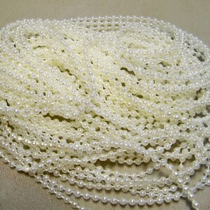May include: A large spool of white pearl-like beads. The beads are strung together on a clear thread.