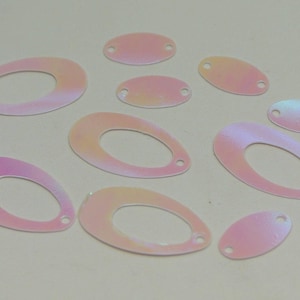 May include: A collection of iridescent sequins in various shapes and sizes. The sequins include oval and teardrop shapes, each with a small hole for sewing. The colors shift from pink to yellow, creating a shimmering effect. These are ideal for embellishments.