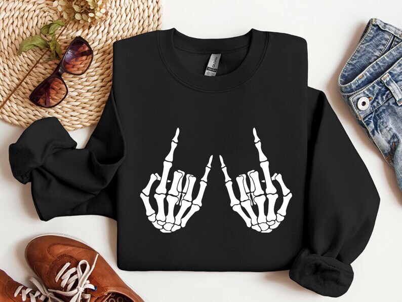 May include: A black long-sleeve crewneck sweatshirt featuring a white graphic print of two skeleton hands positioned to display the rock and roll hand sign. The sweatshirt has a ribbed collar, cuffs, and hem, with a standard fit and solid black fabric.